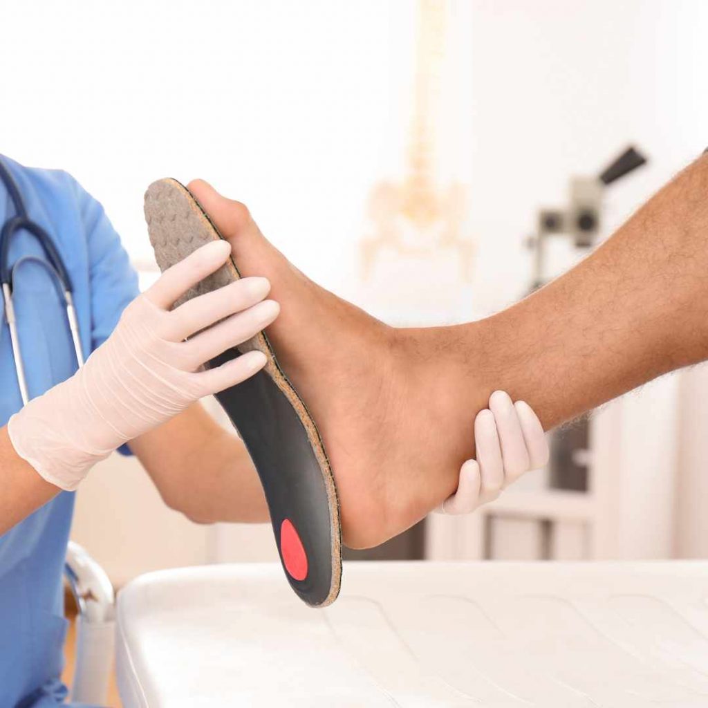 Læge eller fysioterapeut tilpasser en ortopædisk indlægssål til en patient med fodsmerter.