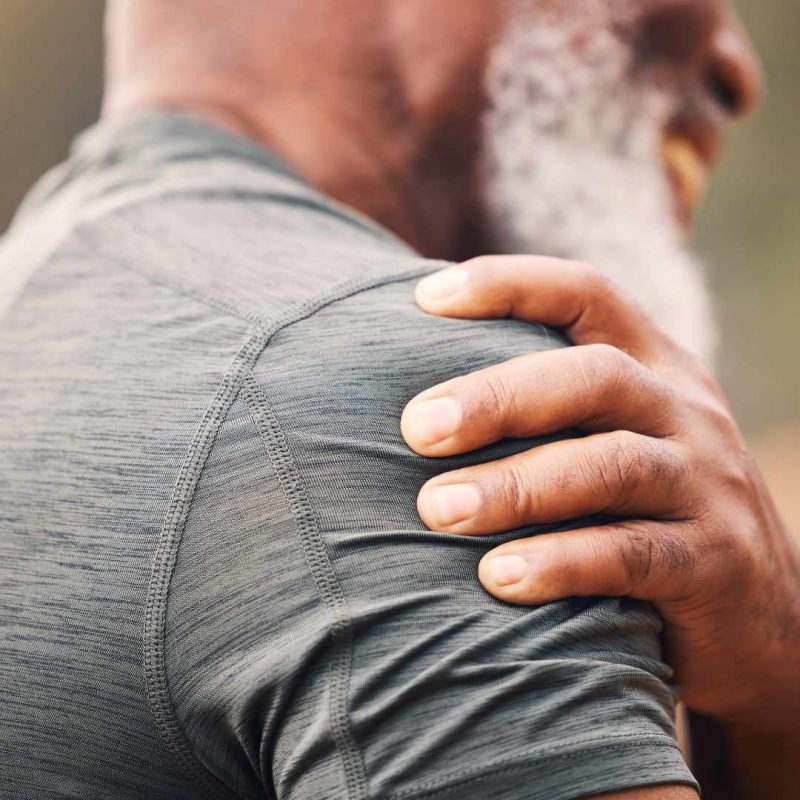 Ældre mand med hånd på skulderen som udviser smerte, et muligt tegn på inflammation i skulder.
